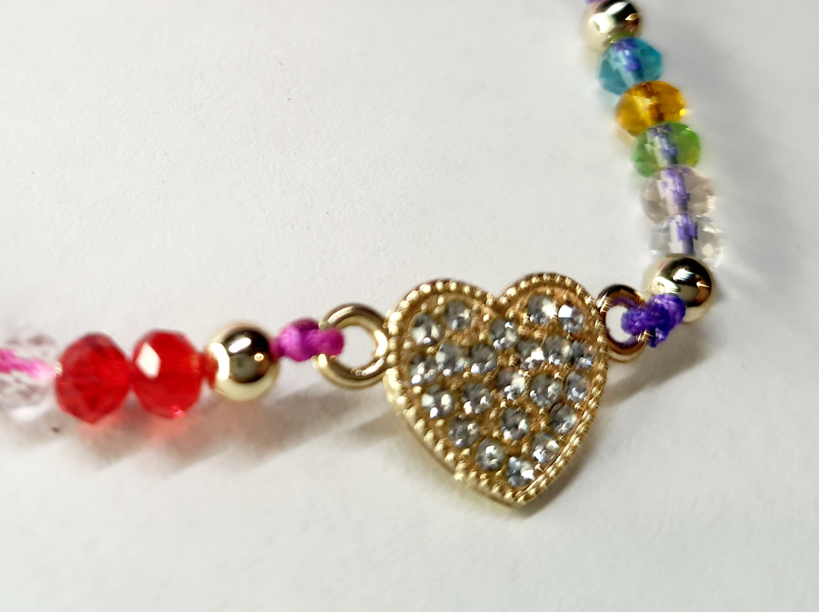 Bransoletka z sercem wysadzanym cyrkoniami na różowo-fioletowym sznurku z kolorowymi koralikami. Delikatna, kolorowa biżuteria w stylu boho, romantyczna i radosna. Wodoodporne, hipoalergiczne, jakość premium. Rouge Bizu.