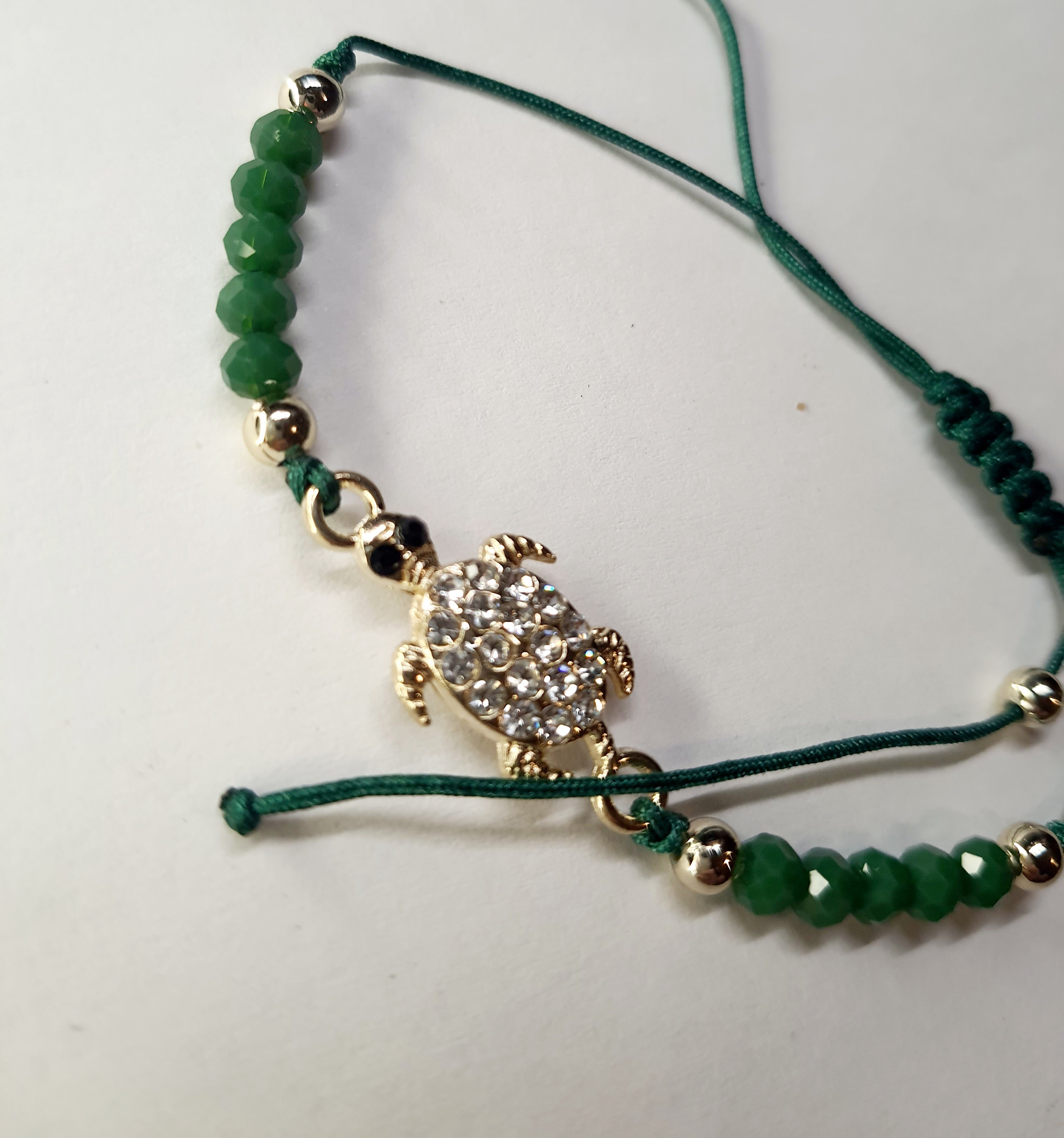 Bransoletka z zawieszką w kształcie żółwia wysadzanego cyrkoniami na zielonym sznurku z zielonymi koralikami. Styl boho, talizman szczęścia i harmonii. Wodoodporne, hipoalergiczne, jakość premium. Rouge Bizu.