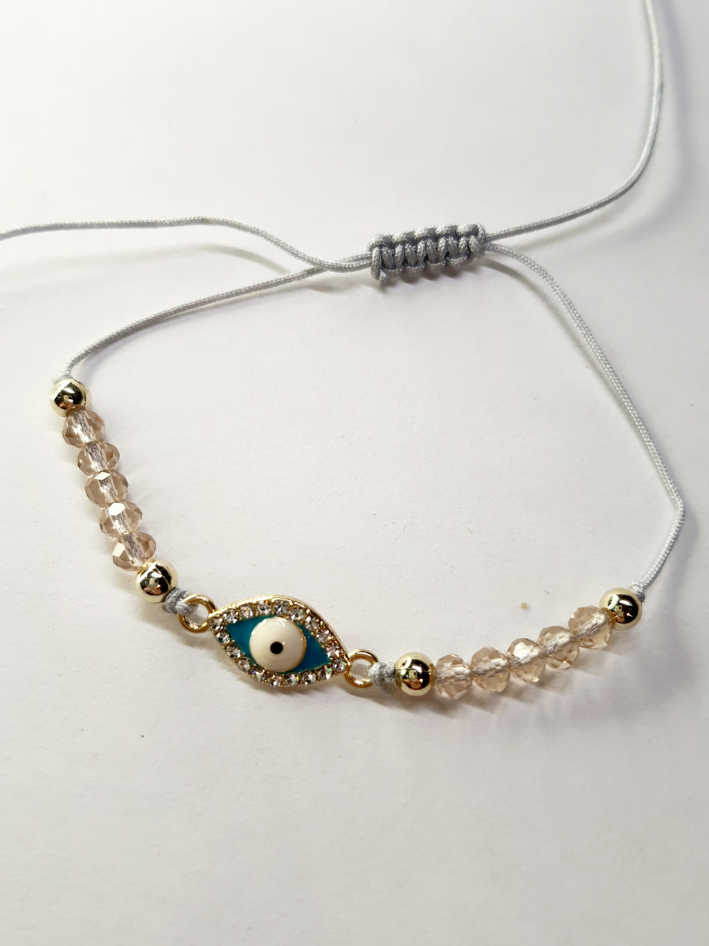 Bransoletka z turkusowym okiem proroka w złotej oprawie wysadzanej cyrkoniami, na różowym sznurku z przezroczystymi koralikami. Delikatna, ochronna biżuteria w stylu boho. Wodoodporne, hipoalergiczne, jakość premium. Rouge Bizu.
