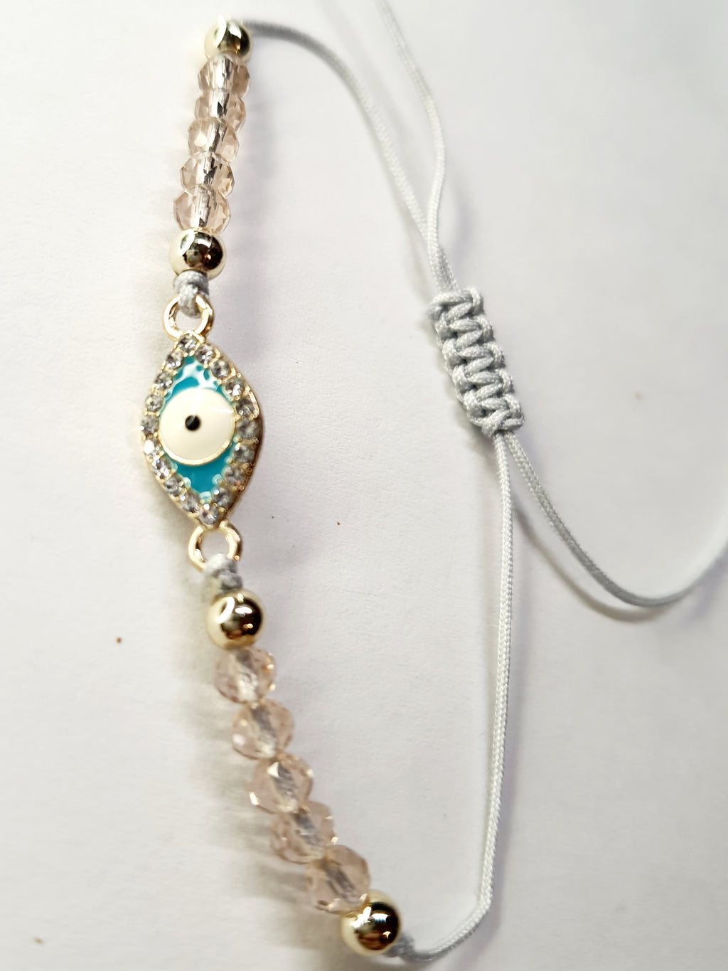 Bransoletka z turkusowym okiem proroka w złotej oprawie wysadzanej cyrkoniami, na różowym sznurku z przezroczystymi koralikami. Delikatna, ochronna biżuteria w stylu boho. Wodoodporne, hipoalergiczne, jakość premium. Rouge Bizu.