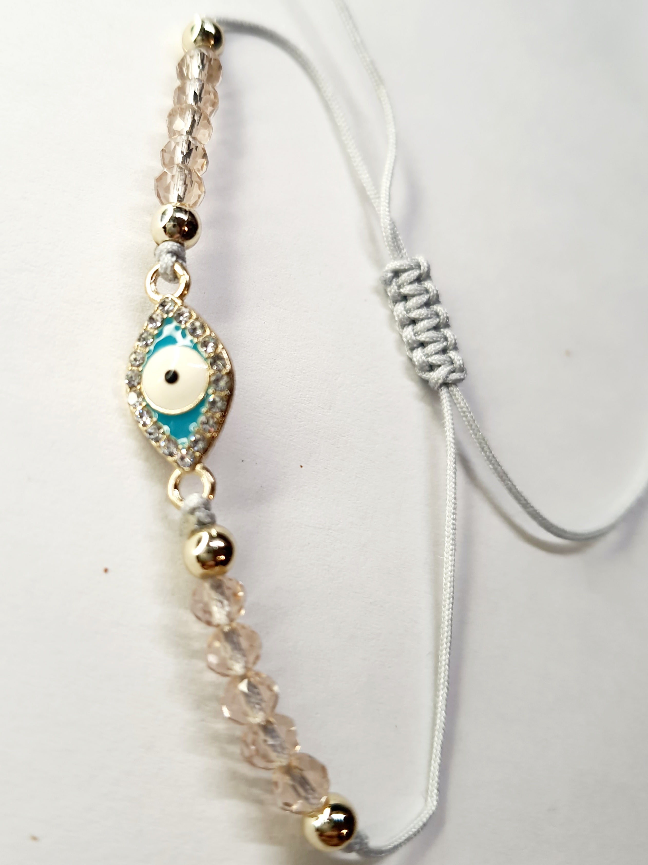 Bransoletka z turkusowym okiem proroka w złotej oprawie wysadzanej cyrkoniami, na różowym sznurku z przezroczystymi koralikami. Delikatna, ochronna biżuteria w stylu boho. Wodoodporne, hipoalergiczne, jakość premium. Rouge Bizu.