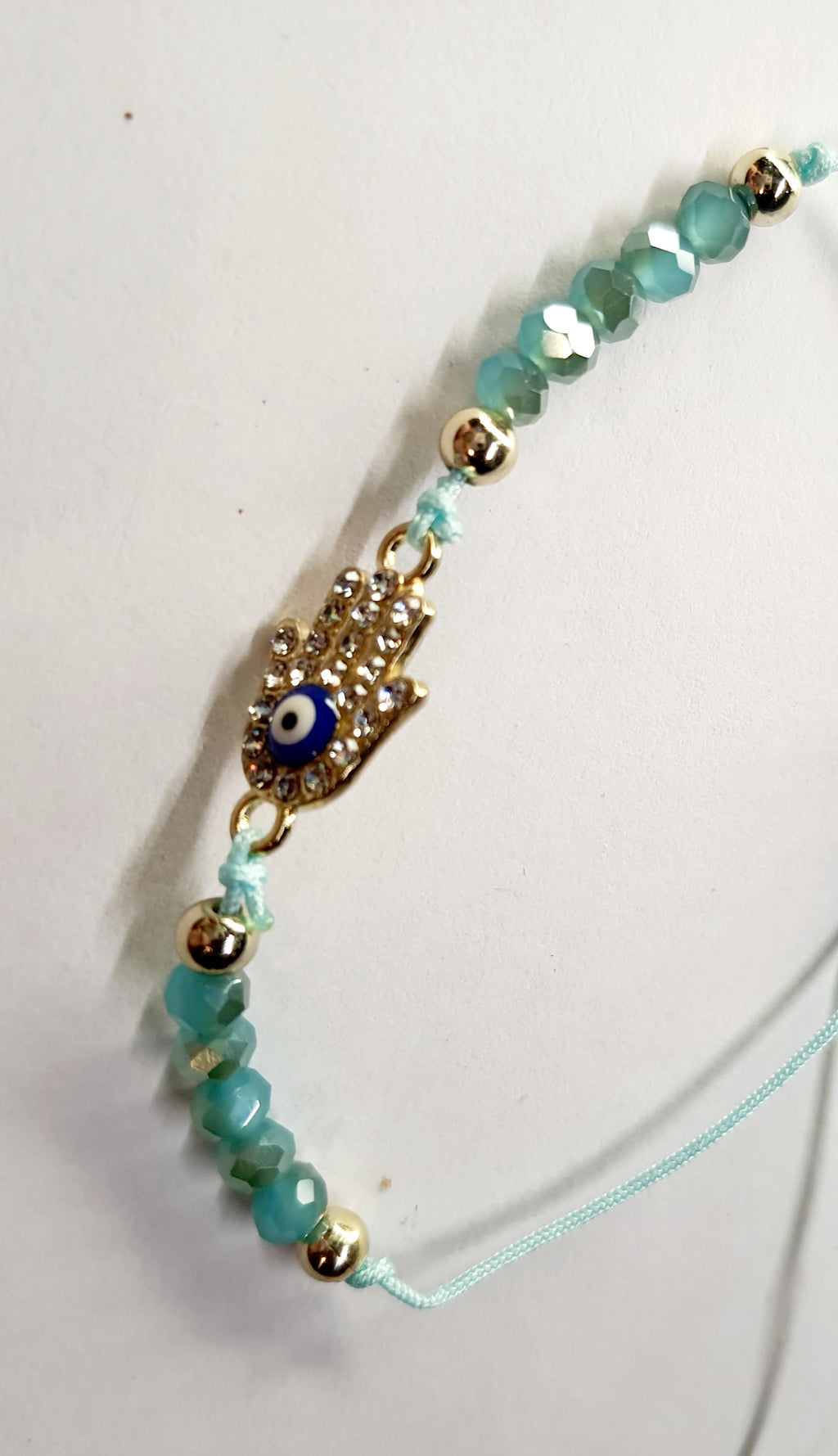Bransoletka z dłonią Fatimy (Hamsa) wysadzaną cyrkoniami i okiem proroka, na miętowym sznurku z miętowymi koralikami. Delikatna, ochronna biżuteria w stylu boho. Wodoodporne, hipoalergiczne, jakość premium. Rouge Bizu.
