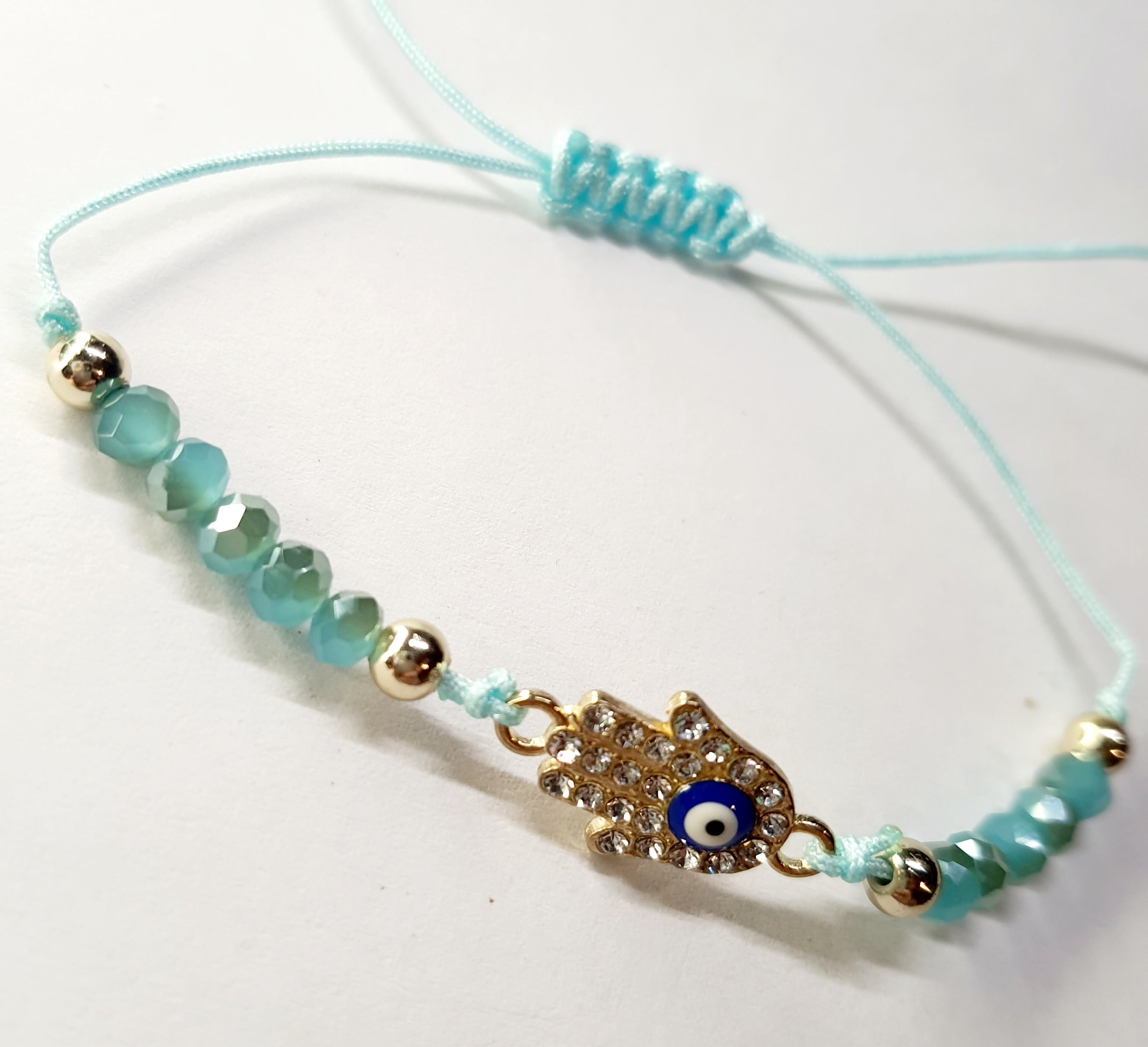 Bransoletka z dłonią Fatimy (Hamsa) wysadzaną cyrkoniami i okiem proroka, na miętowym sznurku z miętowymi koralikami. Delikatna, ochronna biżuteria w stylu boho. Wodoodporne, hipoalergiczne, jakość premium. Rouge Bizu.