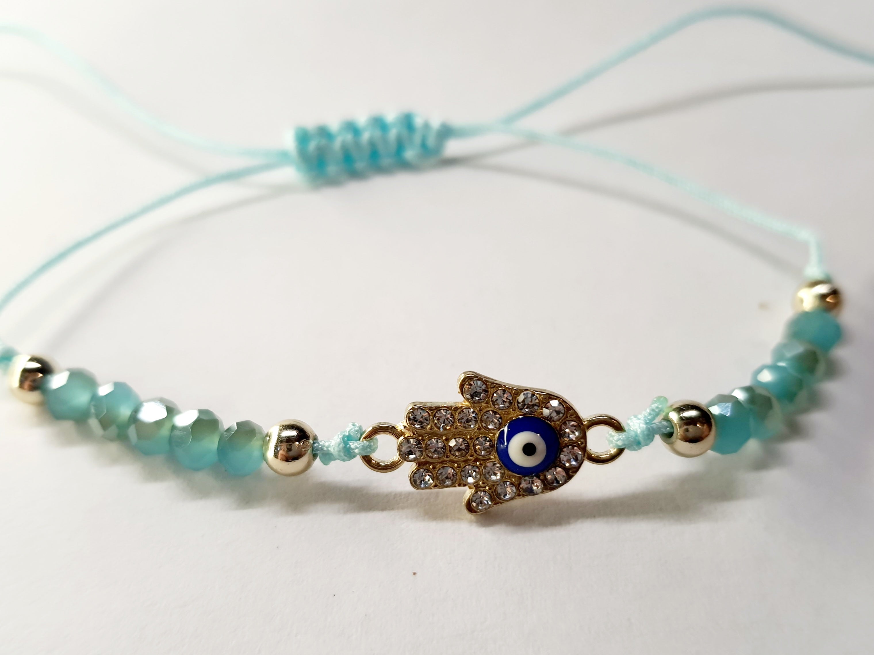 Bransoletka z dłonią Fatimy (Hamsa) wysadzaną cyrkoniami i okiem proroka, na miętowym sznurku z miętowymi koralikami. Delikatna, ochronna biżuteria w stylu boho. Wodoodporne, hipoalergiczne, jakość premium. Rouge Bizu.