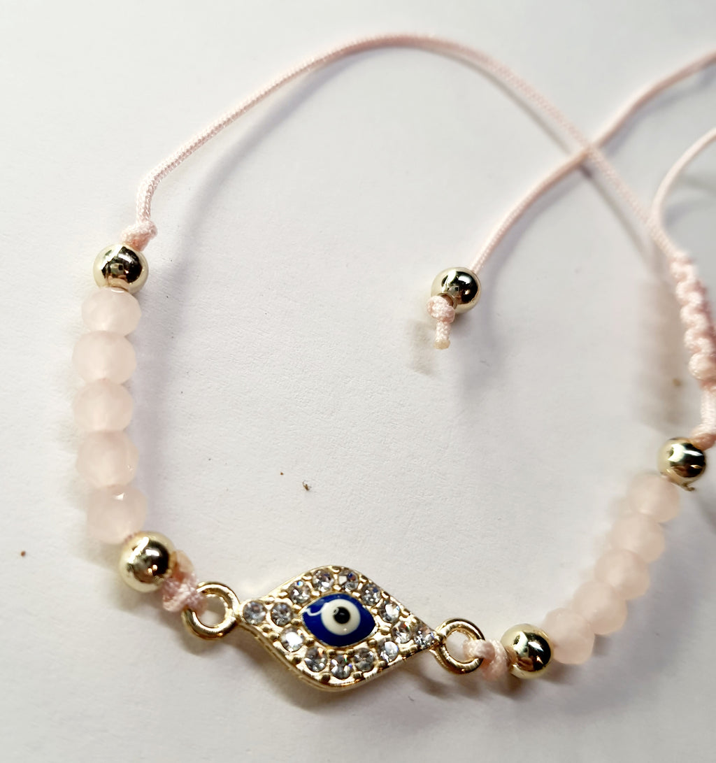 Bransoletka z okiem proroka w złotej oprawie wysadzanej cyrkoniami, na pudroworóżowym sznurku z matowymi różowymi koralikami. Delikatna, kobieca biżuteria ochronna w stylu boho. Wodoodporne, hipoalergiczne, jakość premium. Rouge Bizu.