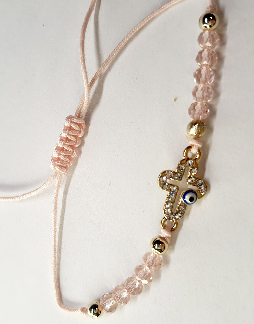 Bransoletka z krzyżem wysadzanym cyrkoniami i okiem proroka, na pudroworóżowym sznurku z różowymi koralikami. Delikatna, elegancka biżuteria ochronna w stylu boho. Wodoodporne, hipoalergiczne, jakość premium. Rouge Bizu.