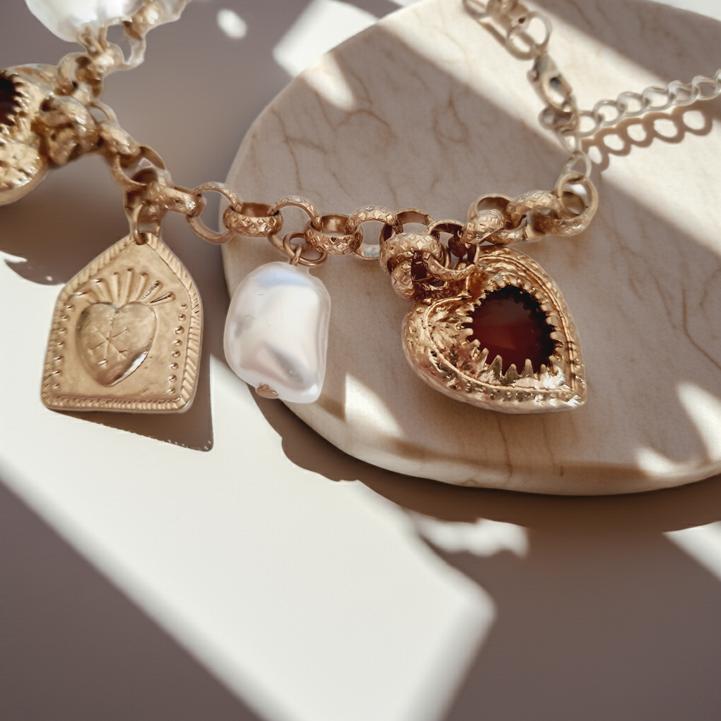 Złota bransoletka w stylu vintage z charmsami: serca, symbole sakralne, perłowe zawieszki. Stal chirurgiczna, długość regulowana 20–28 cm. Klasyka, romantyzm i mistyczna elegancja. Rouge Bizu.

