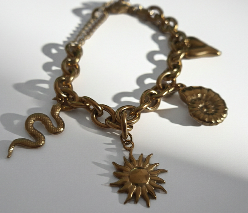 Złota bransoletka w stylu boho z zawieszkami: słońce, muszla, serce, wąż. Regulowana długość 25–30 cm. Talizmaniczna, ze stali nierdzewnej, stal chirurgiczna. Rouge Bizu.
