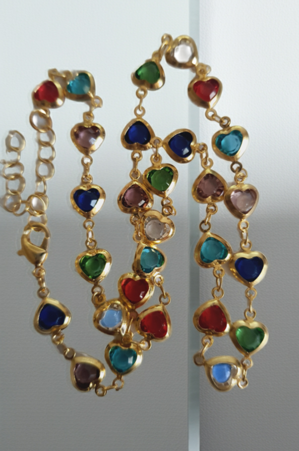 Złoty naszyjnik ze stali chirurgicznej z kolorowymi serduszkami z kryształów w barwach czerwonych, zielonych, niebieskich, fioletowych i turkusowych. Regulowana długość 40–45 cm. Stal chirurgiczna, stal nierdzewna, wodoodporne, hipoalergiczne, jakość premium. RougeBizu.