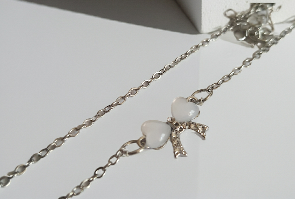 Srebrny naszyjnik ze stali nierdzewnej – stal chirurgiczna, wodoodporny, hipoalergiczny, jakość premium. Zawieszka w kształcie kokardki z dwóch serc, zdobiona kryształkami. Długość łańcuszka 42–49 cm. RougeBizu.