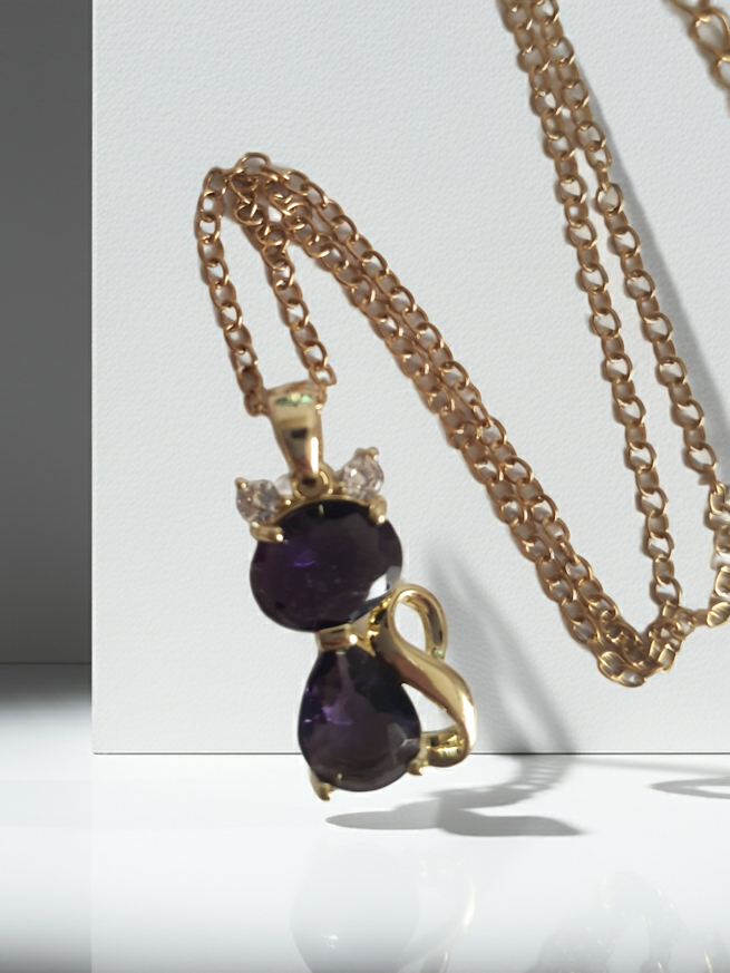 Naszyjnik złoty ze stali nierdzewnej – stal chirurgiczna, wodoodporny, hipoalergiczny, jakość premium. Zawieszka w kształcie kotka z dwóch fioletowych kryształów, ozdobiona złotym detalem i drobnymi cyrkoniami. Długość łańcuszka 40–45 cm. Elegancja i styl RougeBizu.