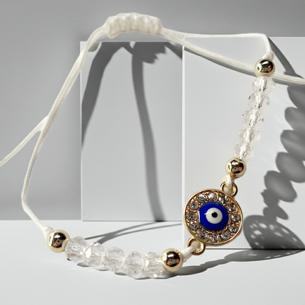 Biała bransoletka na sznurku z niebieskim okiem proroka w złotej oprawie wysadzanej cyrkoniami, z przezroczystymi koralikami. Delikatna, ochronna biżuteria w stylu boho. Wodoodporne, hipoalergiczne, jakość premium. Rouge Bizu.