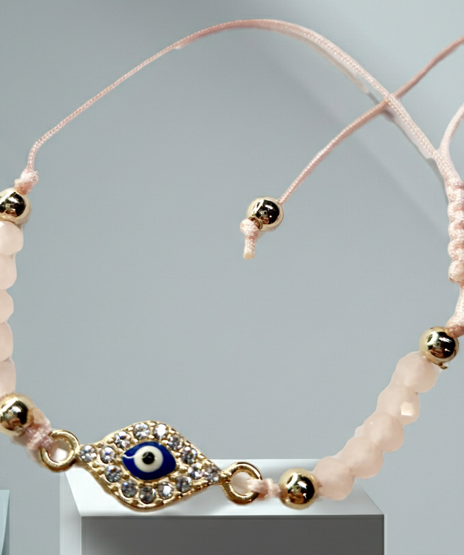 Bransoletka z okiem proroka w złotej oprawie wysadzanej cyrkoniami, na pudroworóżowym sznurku z matowymi różowymi koralikami. Delikatna, kobieca biżuteria ochronna w stylu boho. Wodoodporne, hipoalergiczne, jakość premium. Rouge Bizu.
