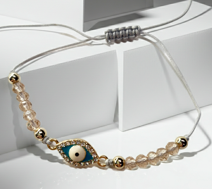 Bransoletka z turkusowym okiem proroka w złotej oprawie wysadzanej cyrkoniami, na różowym sznurku z przezroczystymi koralikami. Delikatna, ochronna biżuteria w stylu boho. Wodoodporne, hipoalergiczne, jakość premium. Rouge Bizu.