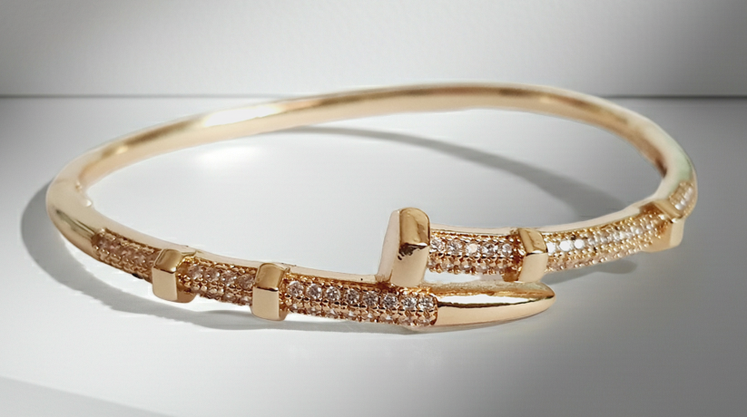 Złota bransoletka sztywna o średnicy 6 cm, zdobiona białymi cyrkoniami, nowoczesny elegancki design, stal nierdzewna. Rouge Bizu.
