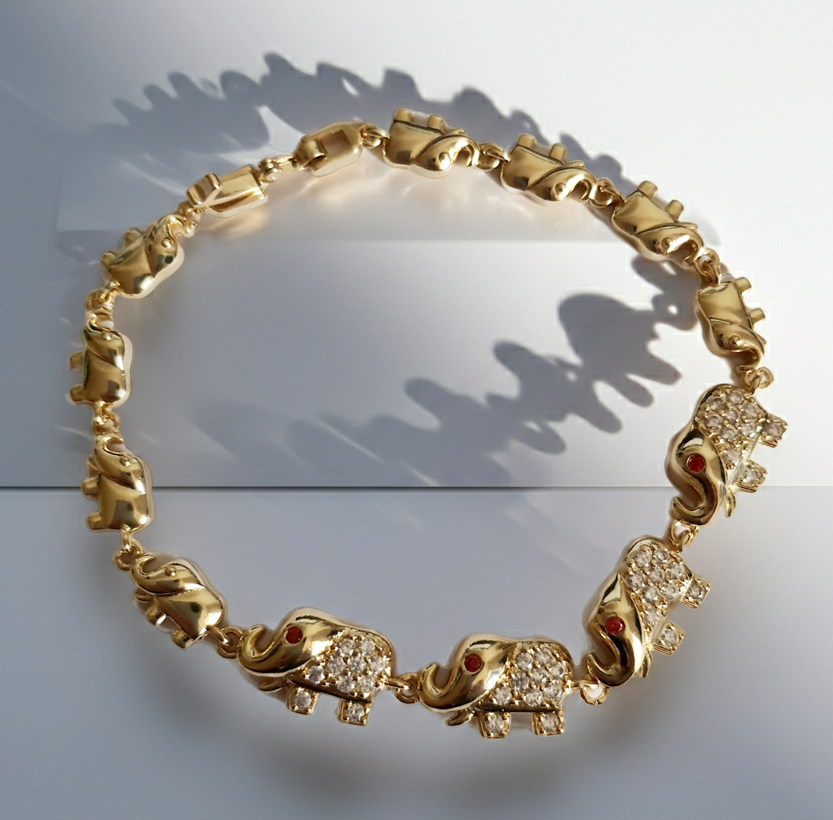 Bransoletka ze stali nierdzewnej w kolorze złota z motywem słoni, zdobiona cyrkoniami i czerwonymi oczkami. Symbol szczęścia, długość 20 cm. Rouge Bizu.