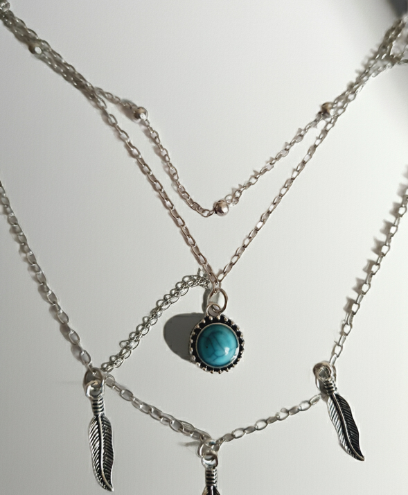 Srebrny potrójny naszyjnik ze stali chirurgicznej – jeden łańcuszek z piórkami, drugi z turkusowym kamieniem, trzeci z kuleczkami. Regulowana długość 39–45 cm. Stal chirurgiczna, stal nierdzewna, wodoodporne, hipoalergiczne, jakość premium. RougeBizu.