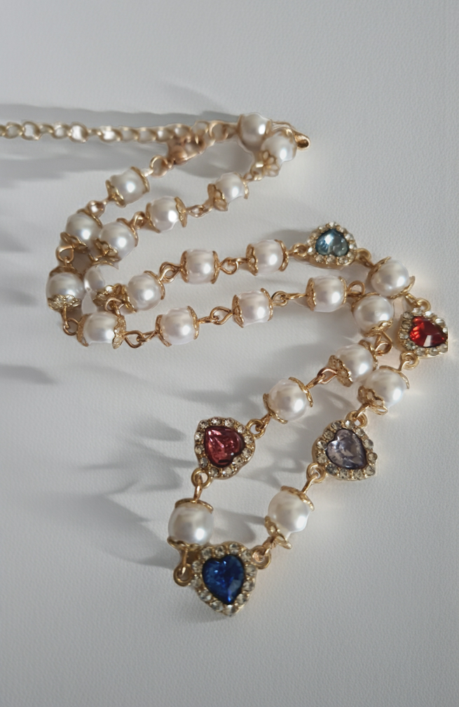 Naszyjnik złoty ze stali nierdzewnej – stal chirurgiczna, wodoodporny, hipoalergiczny, jakość premium. Perły syntetyczne i zawieszki w kształcie kolorowych serc (czerwony, niebieski, różowy, fioletowy) zdobione cyrkoniami. Długość 40–49 cm. RougeBizu.