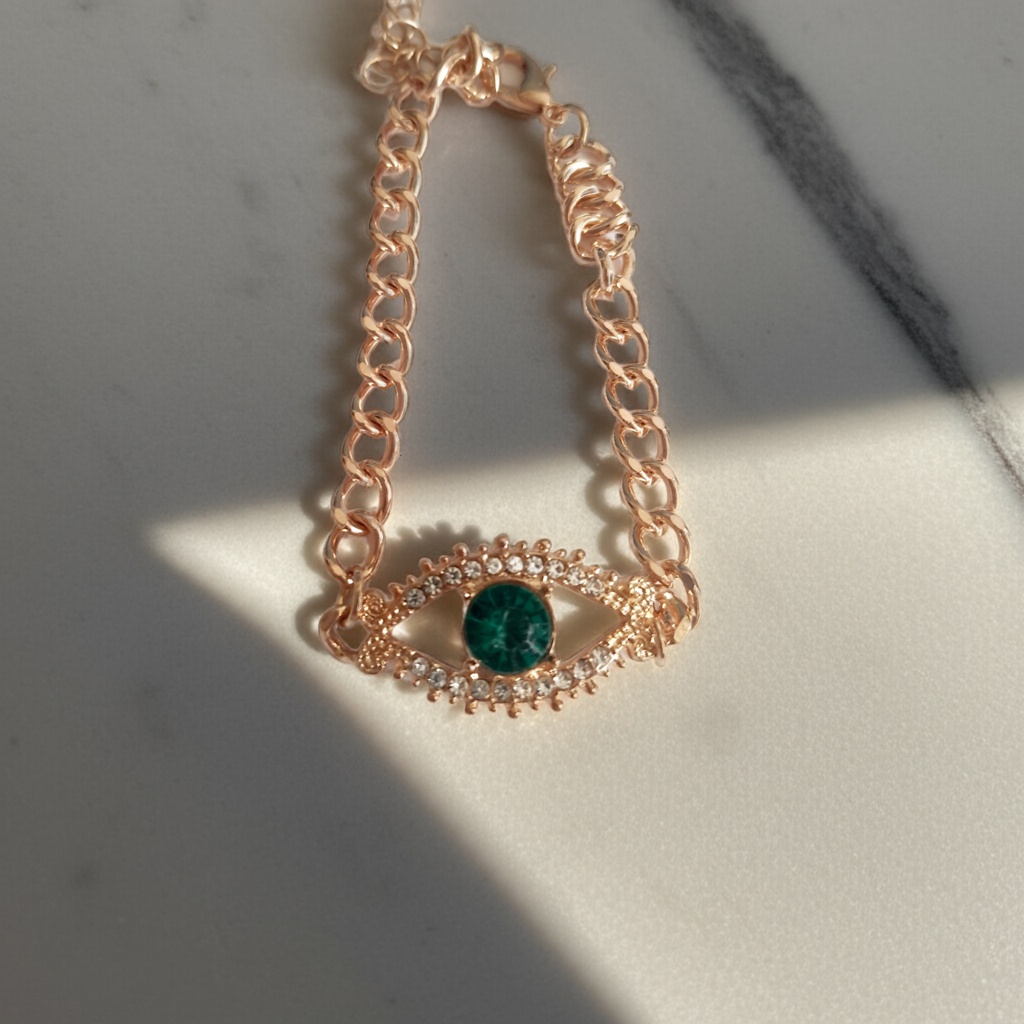 Bransoletka damska o długości 25–30 cm, złota, wykonana ze stali nierdzewnej. Ozdobiona motywem ochronnego oka z zieloną cyrkonią w centrum i białymi kamieniami wokół. Styl glamour z symbolicznym akcentem. Rouge Bizu.

