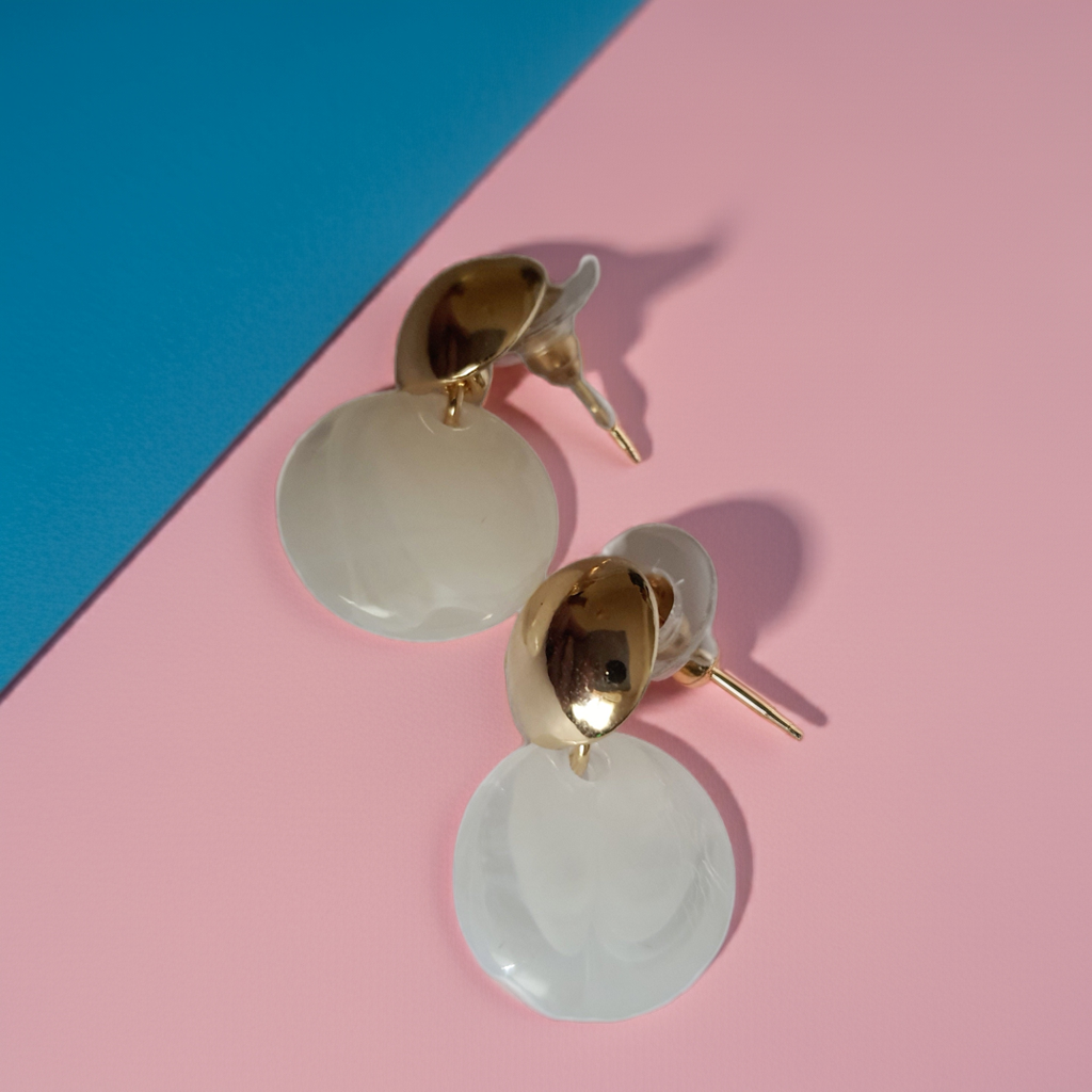 „Złote kolczyki ze stali nierdzewnej o długości 2,5 cm, z perłowym dyskiem zawieszonym na złotym sztyfcie, minimalistyczne i eleganckie – Rouge Bizu.”