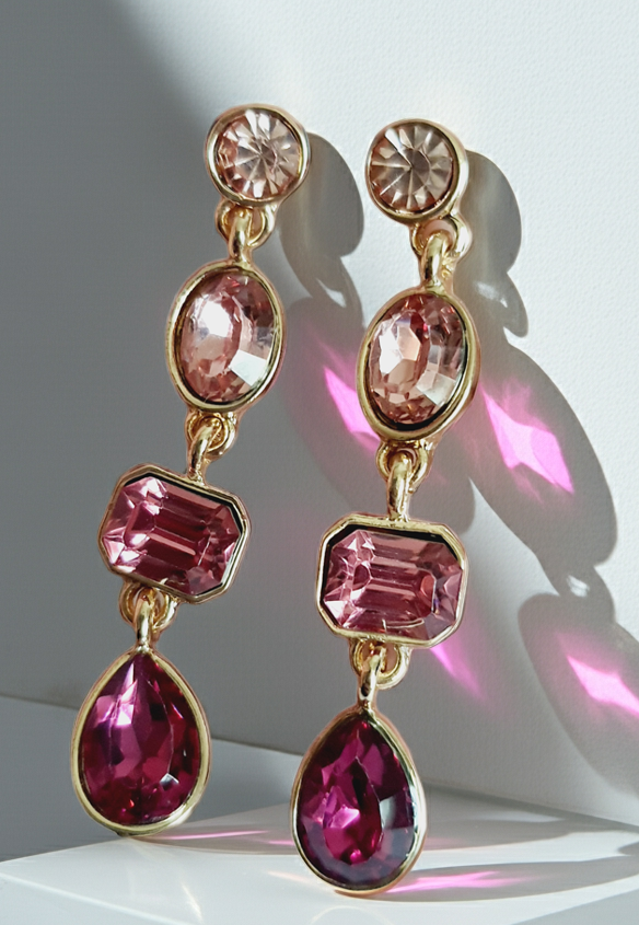 Długie kolczyki wiszące ze stali nierdzewnej w kolorze złota, z różowymi kryształami w kształcie owalu, prostokąta i kropli. Długość 4,5 cm. Styl glamour, elegancki. Rouge Bizu.