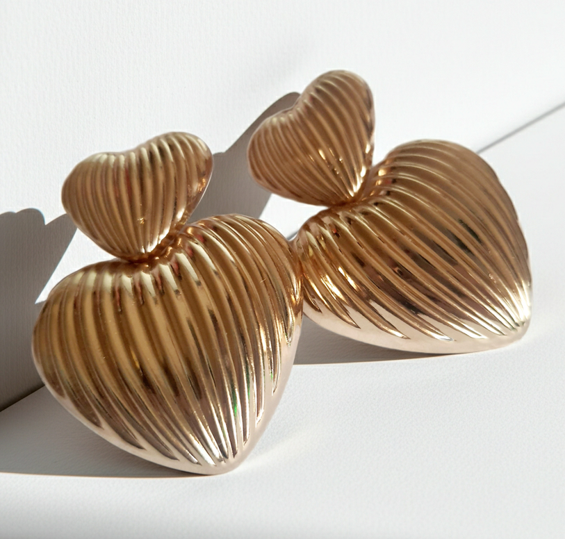 Złote kolczyki w kształcie serc, duże i eleganckie, ze żłobieniami nadającymi im wyjątkowego blasku. Wykonane ze stali nierdzewnej. Rouge Bizu.