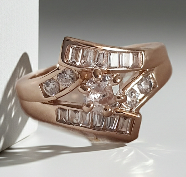 Pierścionek damski ze stali nierdzewnej, złoty, rozmiar 19 mm, zdobiony rzędami prostokątnych cyrkonii i centralnym okrągłym kamieniem, luksusowy styl glamour, Rouge Bizu.