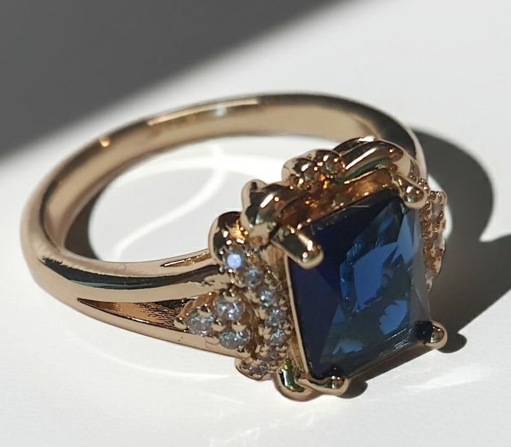 Złoty pierścionek ze stali nierdzewnej z granatowym kamieniem w szlifie szmaragdowym i cyrkoniami po bokach w stylu glamour klasycznym. Rozmiar 20 mm. stal chirurgiczna, stal nierdzewna, wodoodporne, hipoalergiczne, jakość premium, RougeBizu.