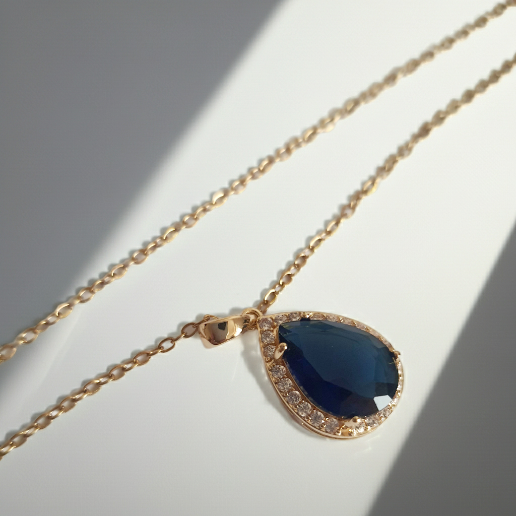 Złoty naszyjnik ze stali chirurgicznej z zawieszką w kształcie łezki z granatowym kamieniem otoczonym cyrkoniami. Regulowana długość 41–47 cm. Stal chirurgiczna, stal nierdzewna, wodoodporne, hipoalergiczne, jakość premium. RougeBizu.