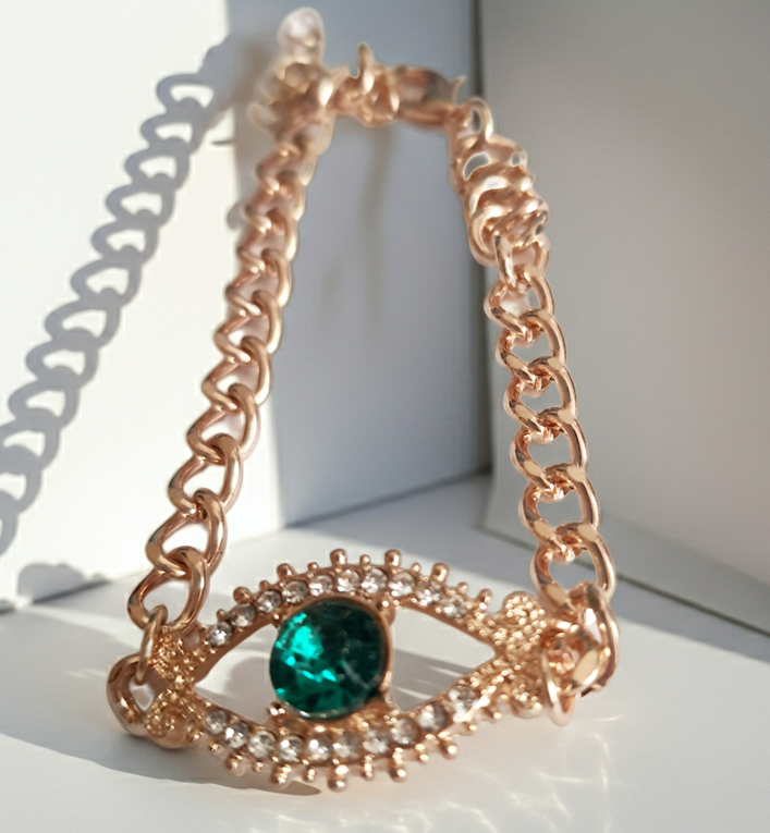 Bransoletka damska o długości 25–30 cm, złota, wykonana ze stali nierdzewnej. Ozdobiona motywem ochronnego oka z zieloną cyrkonią w centrum i białymi kamieniami wokół. Styl glamour z symbolicznym akcentem. Rouge Bizu.
