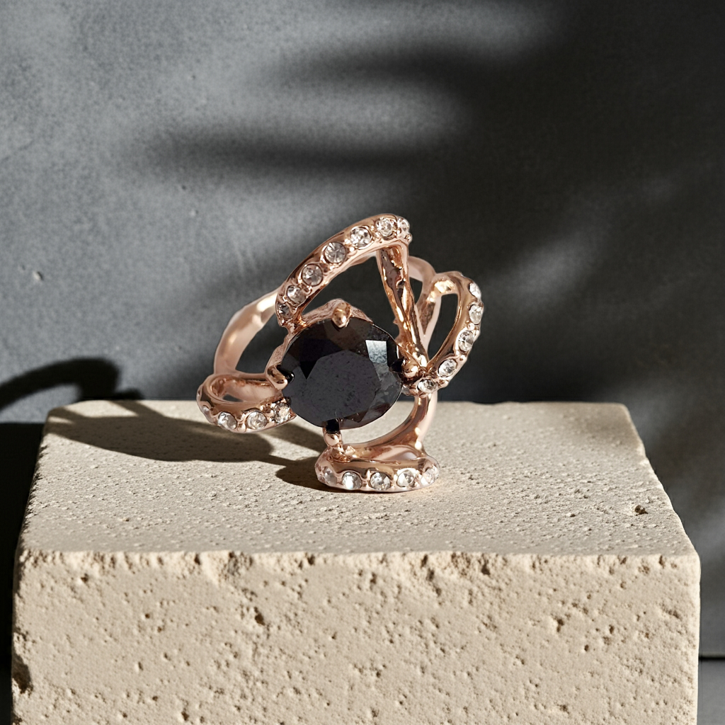 Pierścionek ze złota różowego z dużym czarnym kamieniem w centrum i zdobieniami z drobnych cyrkonii. Styl glamour, rozmiar 18 mm. Elegancki, efektowny, wykonany ze stali chirurgicznej. Rouge Bizu.
