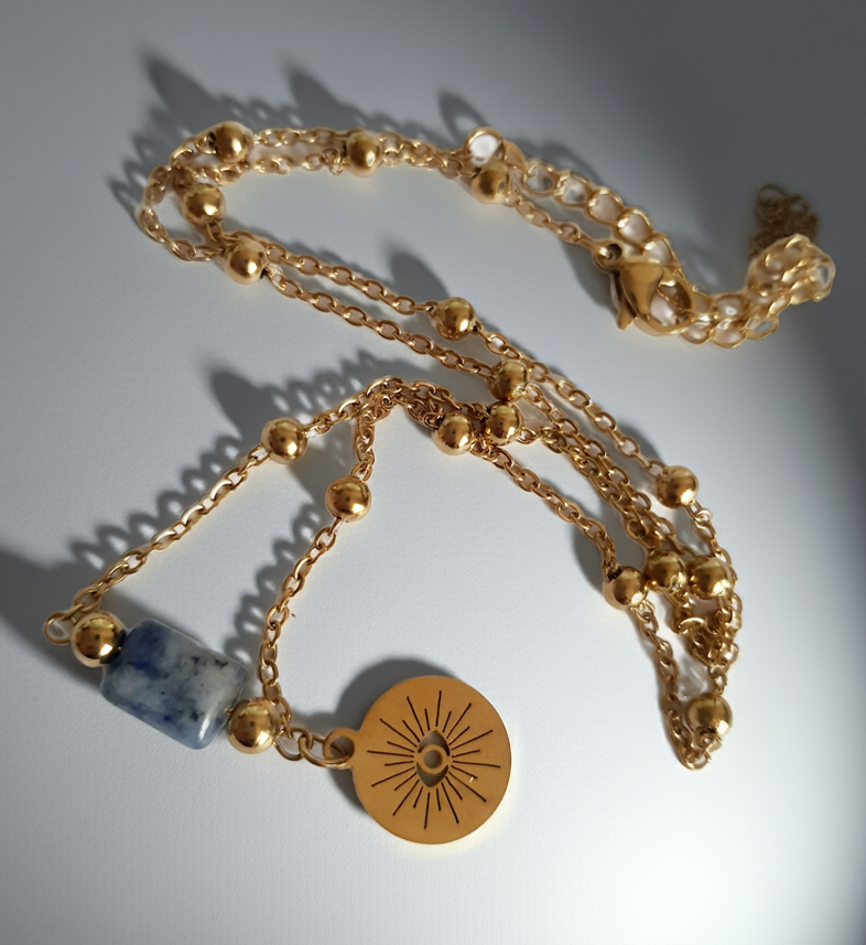 Złoty łańcuszek ze stali nierdzewnej o długości 40–45 cm z granatowym kamieniem i okrągłym talizmanem w kształcie słońca. Styl boho, minimalistyczny, duchowy. Rouge Bizu.
