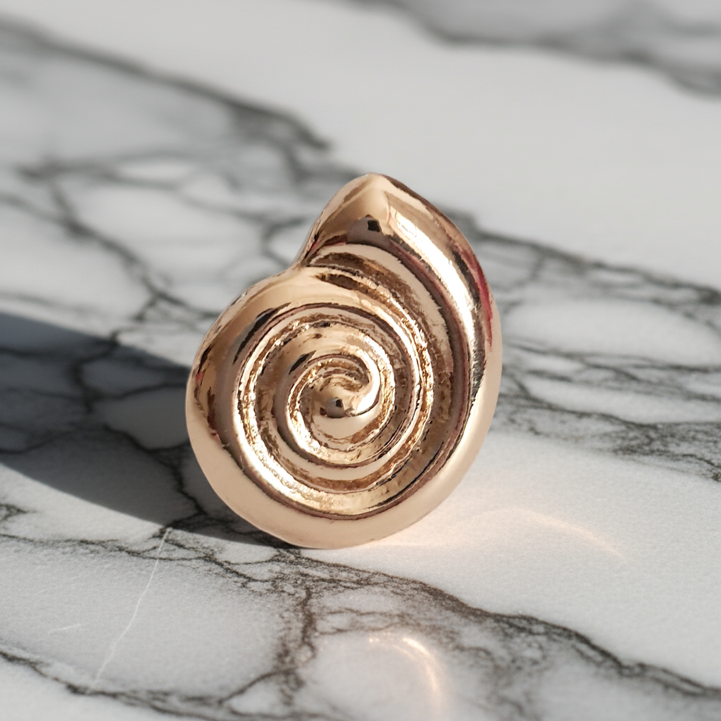 Pierścionek spiralny ze stali nierdzewnej w kolorze żółtego złota, z błyszczącym wykończeniem i efektownym, hipnotyzującym kształtem spirali. Styl minimalistyczny z nutą artystycznej ekstrawagancji. Regulowany rozmiar. Rouge Bizu.
